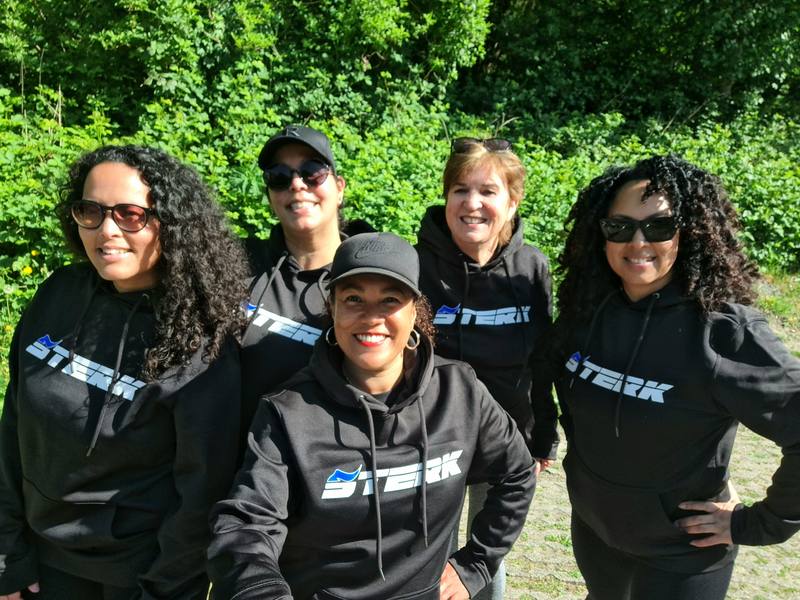 Vijf trainers en leden in zwarte STERK-hoodies, buiten in het groen.