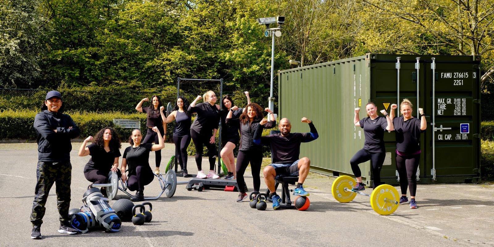 Trainers en leden van STERK zetten hun spierballen op bij de groene STERKBOX-container, met halters, kettlebells, slamballs en een squatrek om zich heen.
