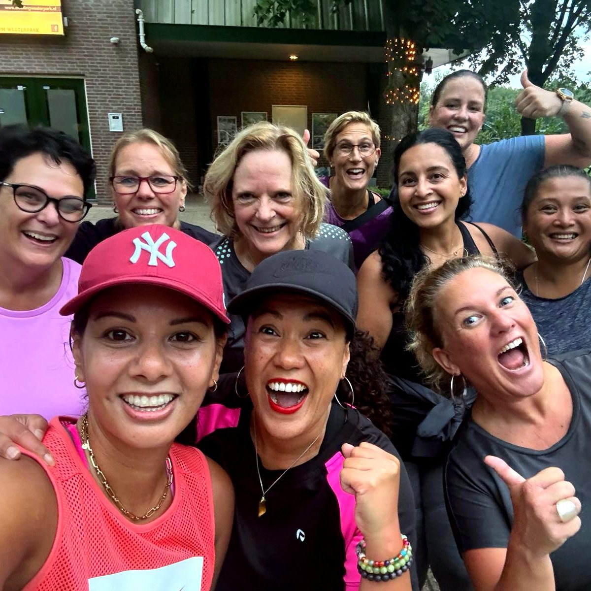 Een groep sportende vrouwen van STERK maakt lachend en juichend een selfie, duimen omhoog.